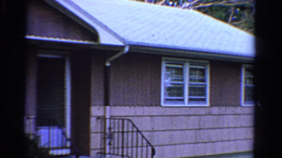 1958 Ontario home-movie frame showing the house entrance, black metal railing, double window, siding, and sloped roofline.