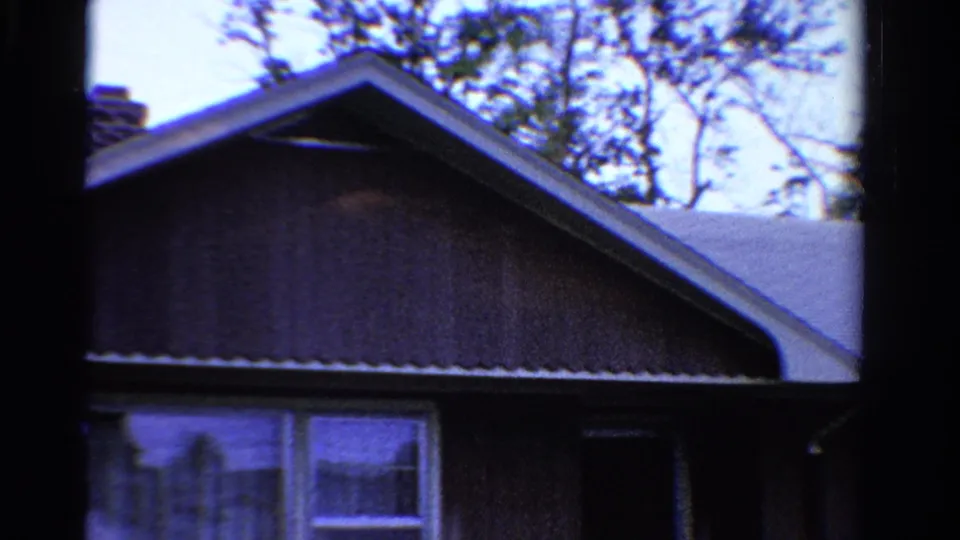 1958 Ontario home-movie frame centered on the house gable, pale roof, brown siding, lower window, trees, and visible film borders.