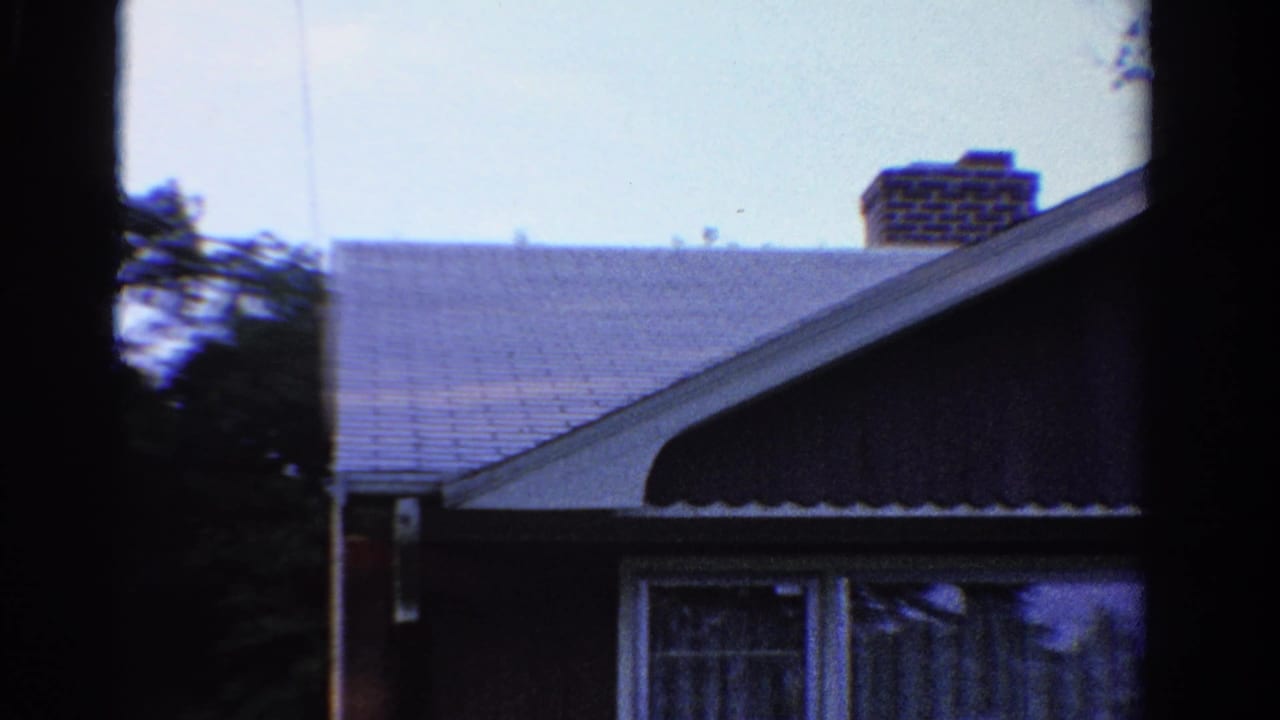 1958 Ontario exterior view of a residential garage and roofline, with windows, chimney, siding, and trees in the background.