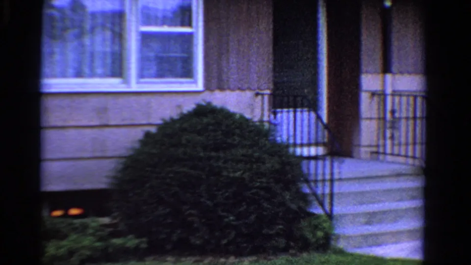 1958 Ontario house exterior showing front steps, metal railing, brown siding, curtained window, shrub, and lawn.