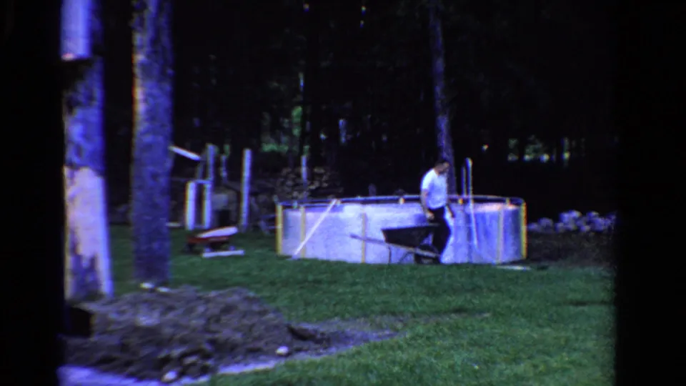 1958 Ontario backyard frame showing a man near a temporary above-ground pool, lawn, trees, and scattered yard materials.