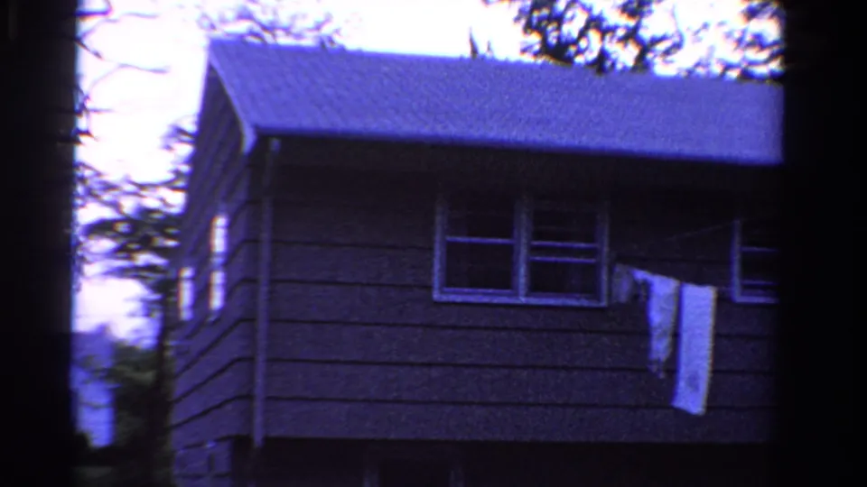 1958 Ontario frame showing a modest house exterior with siding, windows, roofline, and a hanging cloth or linen.