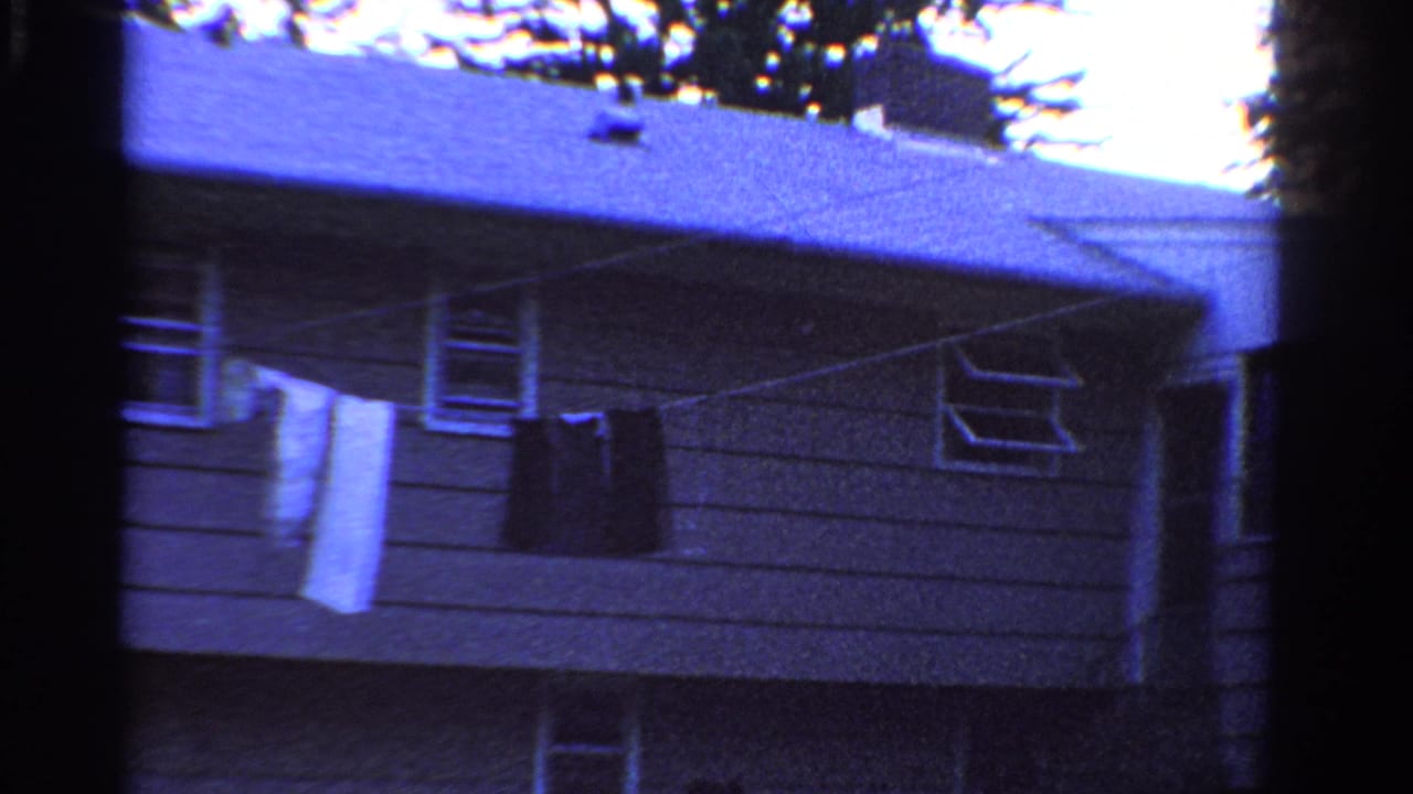 1958 Ontario frame with gray house siding, roof eaves, open windows, and garments drying on a clothesline.