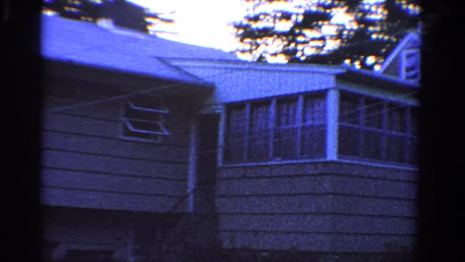 Angled 1958 Ontario home-movie view of a gray house exterior with windows, roofline, and clothesline.