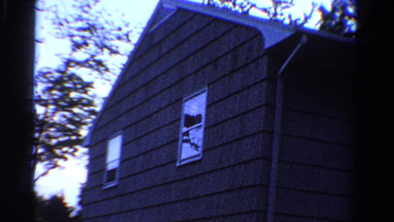 1958 Ontario 8mm frame showing a dark shingled house exterior from below, with white window trim and tree branches overhead.