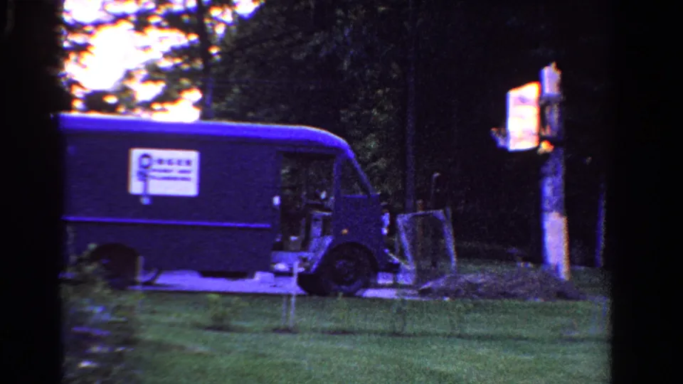 Blue delivery van in a 1958 Ontario backyard, with a bright sign or marker on a wooden post nearby.