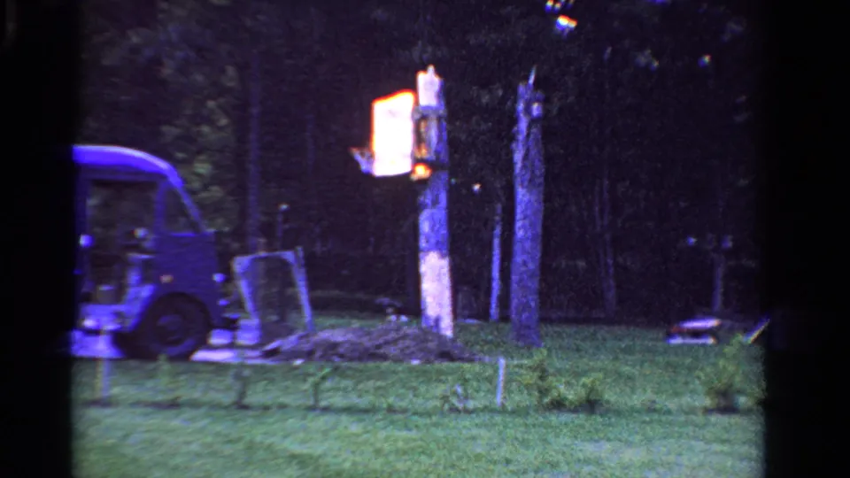 Late frame from the Ontario home movie showing the delivery van partly cropped beside a lawn, trees, and glowing post marker.