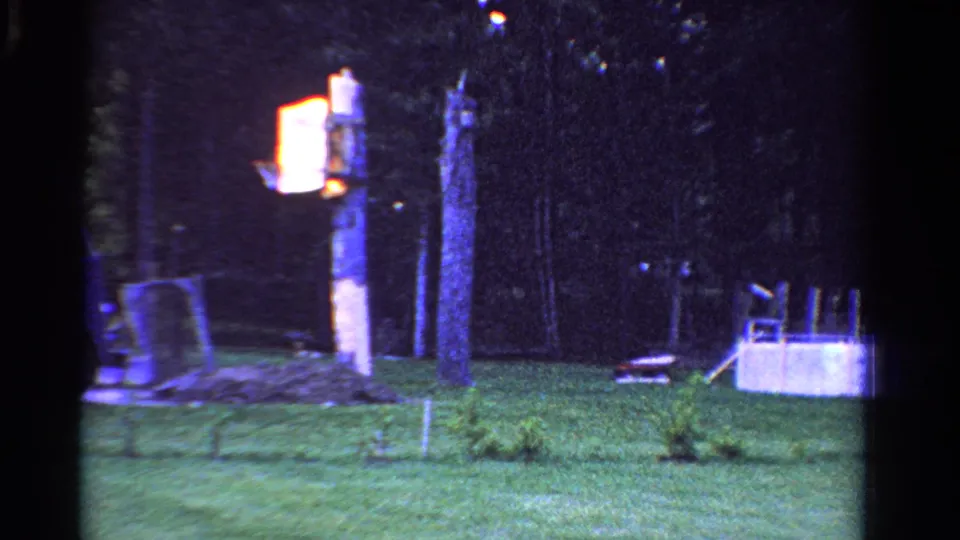 1958 Ontario 8mm frame showing a dusky backyard with grass, trees, a glowing yard light, and a small above-ground pool.