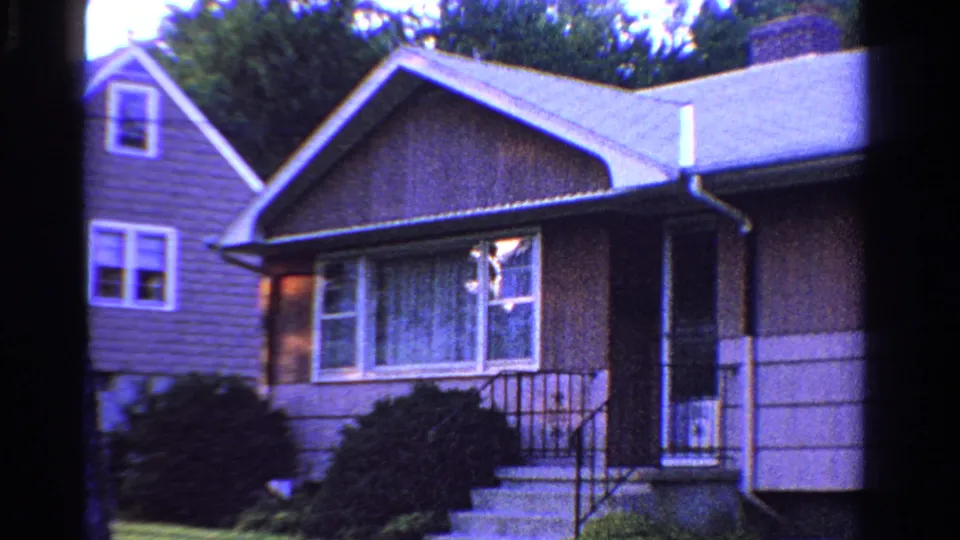 1958 Ontario 8mm frame showing a modest suburban house exterior with siding, front windows, shrubs, steps, and porch railings.
