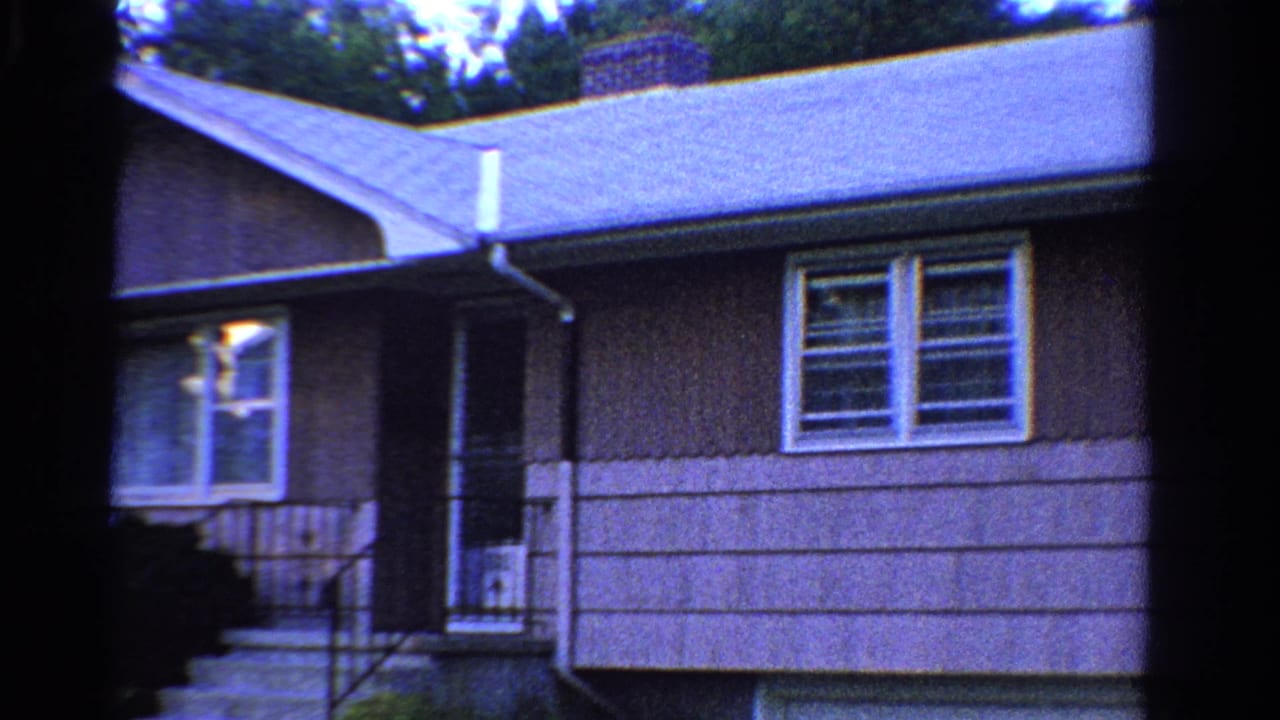 1958 Ontario 8mm frame showing a modest house exterior with porch steps, white-trimmed windows, roofline, and chimney.