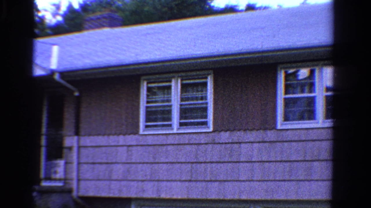 1958 Ontario home-movie frame centered on the house wall, roofline, chimney, downspout, and white-trimmed windows.