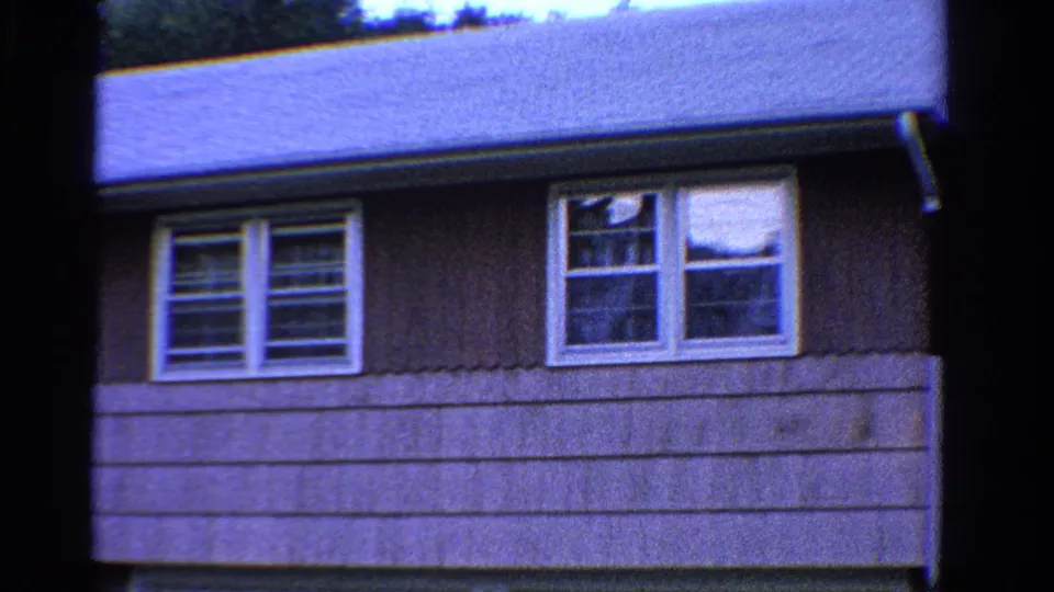 1958 Ontario 8mm frame showing exterior siding beneath the roof edge with two sets of white-trimmed windows.
