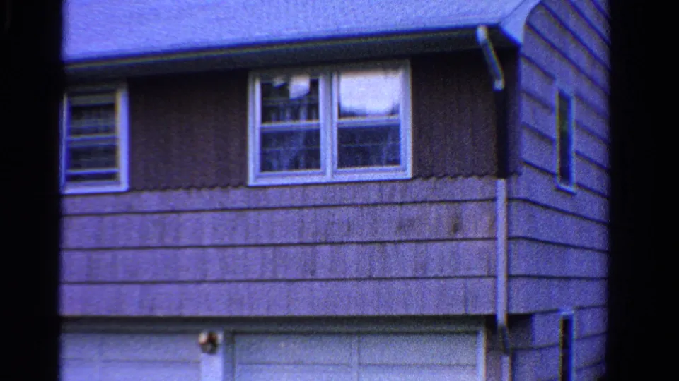 1958 Ontario 8mm frame showing the side portion of the house with windows above a garage door and layered siding.