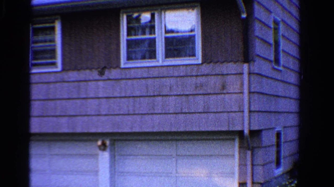 1958 Ontario home-movie frame showing a two-story suburban house facade with horizontal siding, upper windows, and white garage doors.