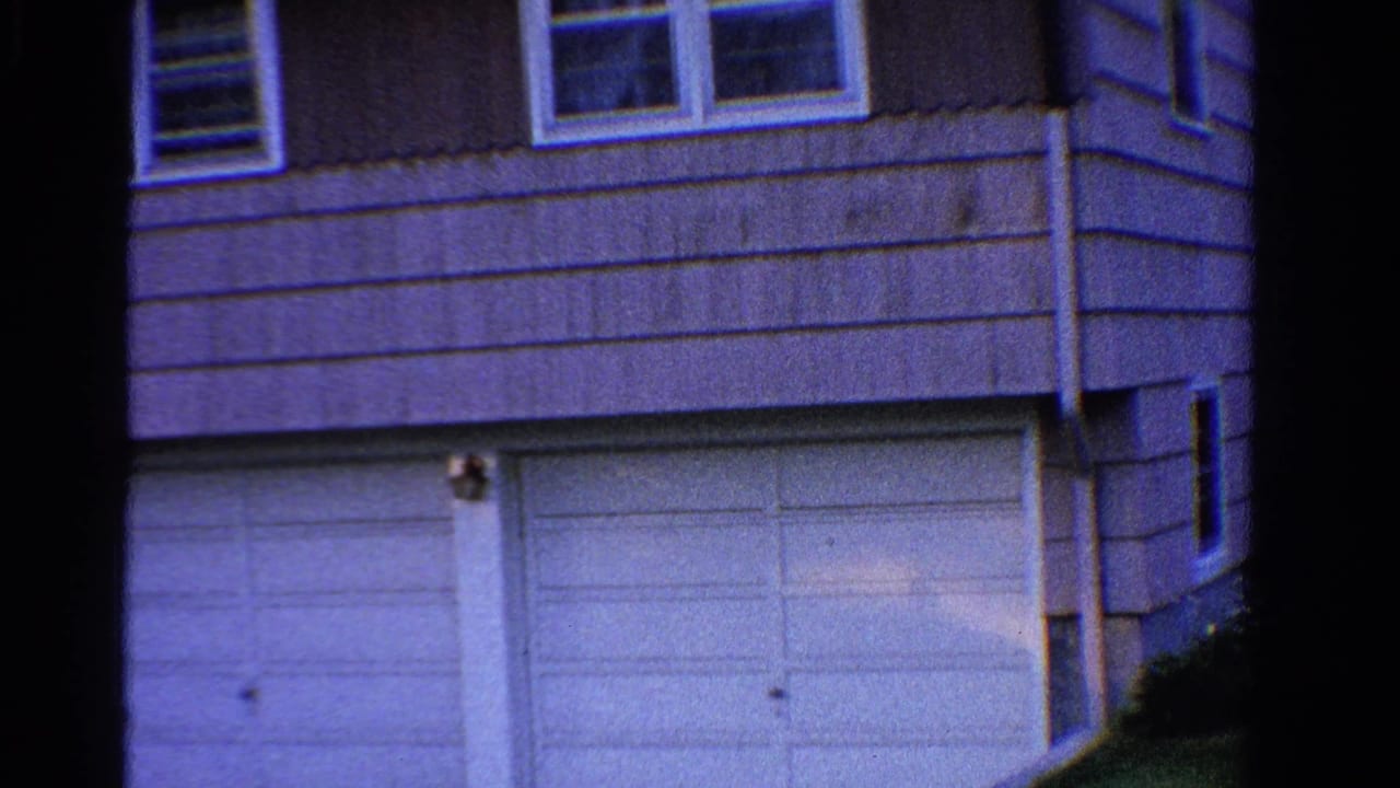 House corner with upper windows, siding, and a large white garage door.