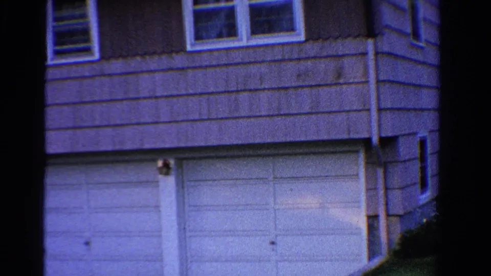 1958 Ontario exterior frame showing the corner of a suburban house, white-framed windows, siding, and a garage door below.