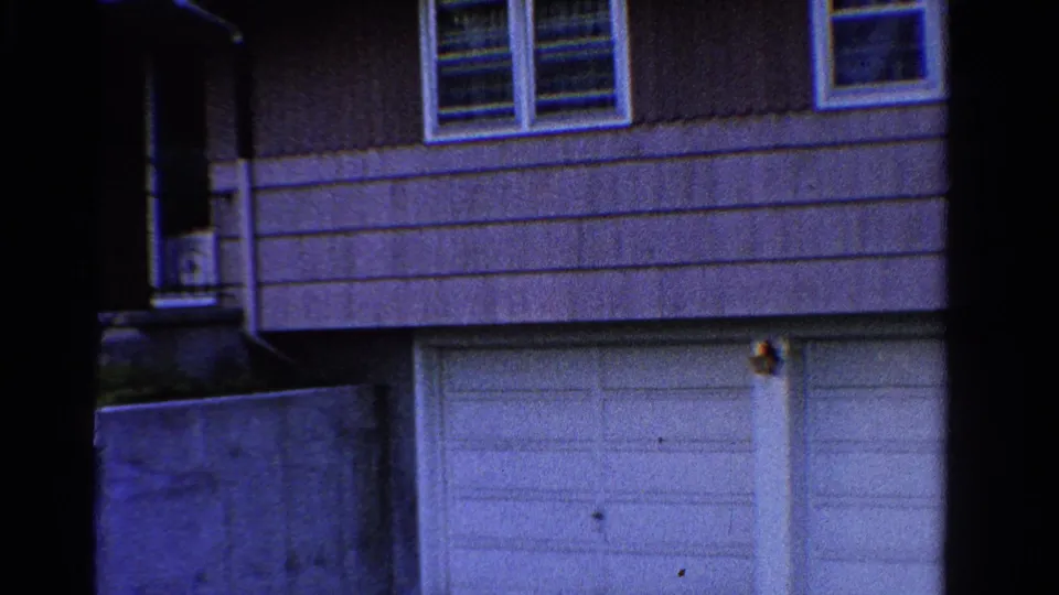 1958 Ontario frame showing the house facade with garage doors, upper windows, a dark entry area, porch steps, and a low concrete wall.