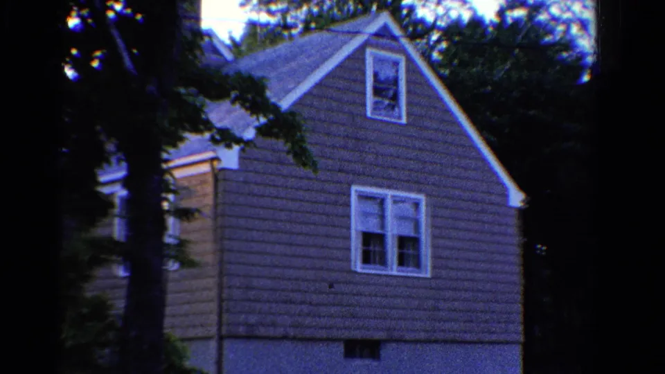 1958 Ontario exterior frame showing a two-story house with gray siding, white trim, and trees around it.
