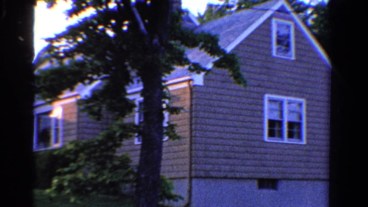 1958 Ontario home-movie view of a light-sided suburban house seen through trees, with grass and windows visible.