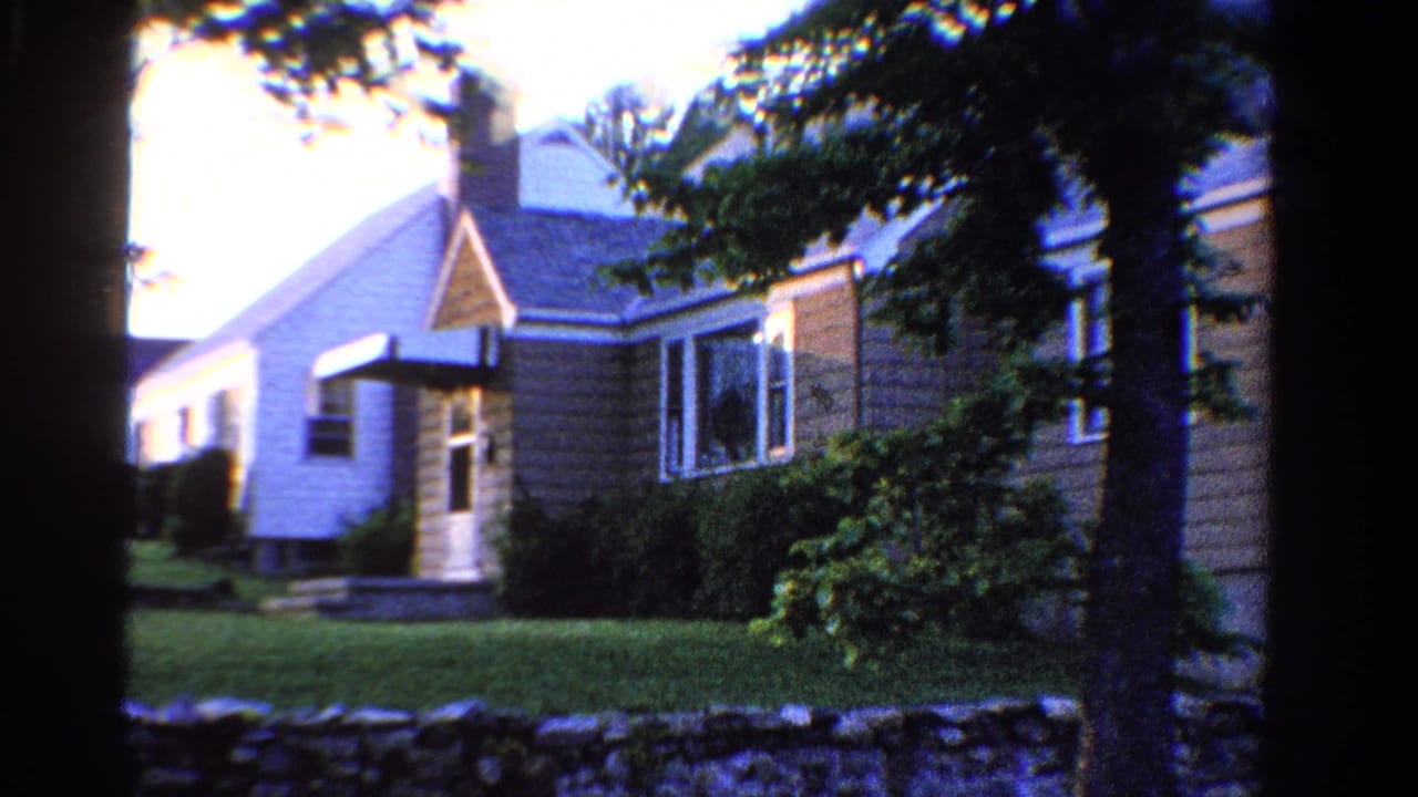 1958 Ontario residential exterior with neighboring houses, trimmed grass, shrubs, trees, and a low stone wall.