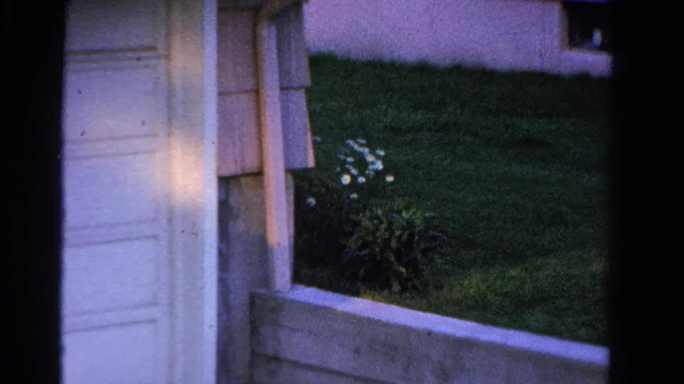 Close home-movie view of a house entrance area in Ontario, with siding, lawn, shrubs, and concrete edging.