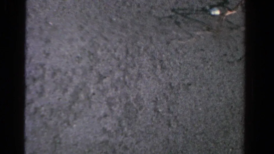 End frame from the 1958 Ontario 8mm clip showing a mostly dark ground surface with visible grain and frame-edge shadows.