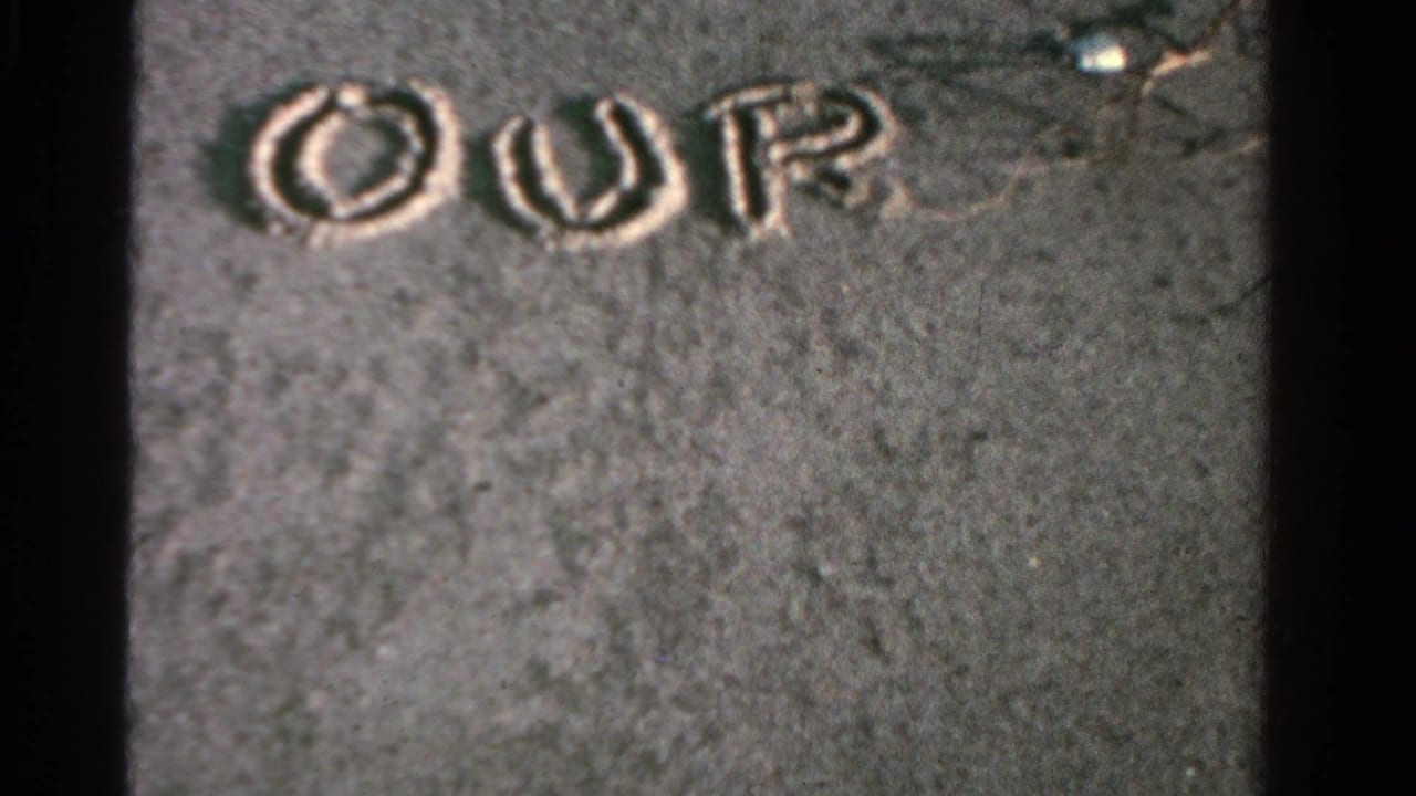 Hand-drawn letters spelling OUR appear in wet sand in this 1958 Ontario home-movie beach frame.