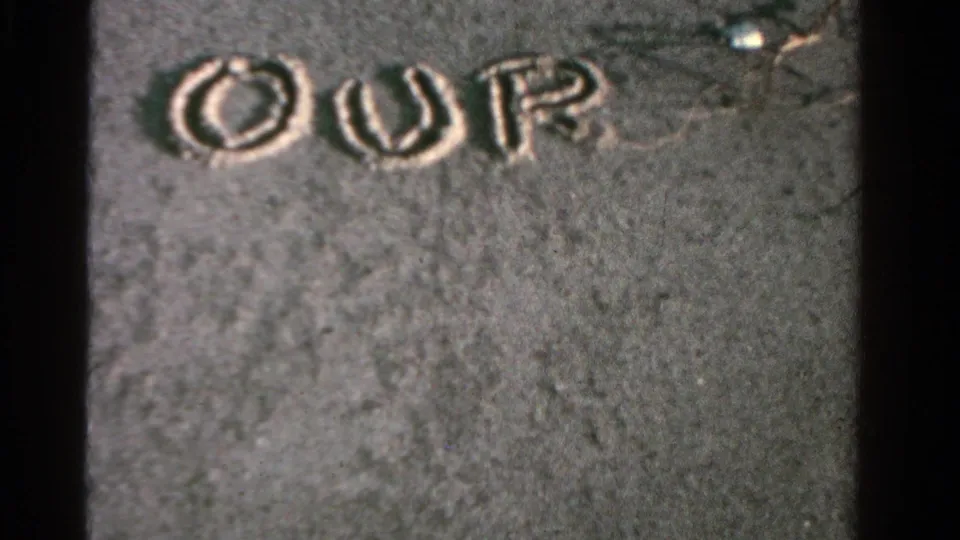 Hand-drawn letters spelling OUR appear in wet sand in this 1958 Ontario home-movie beach frame.