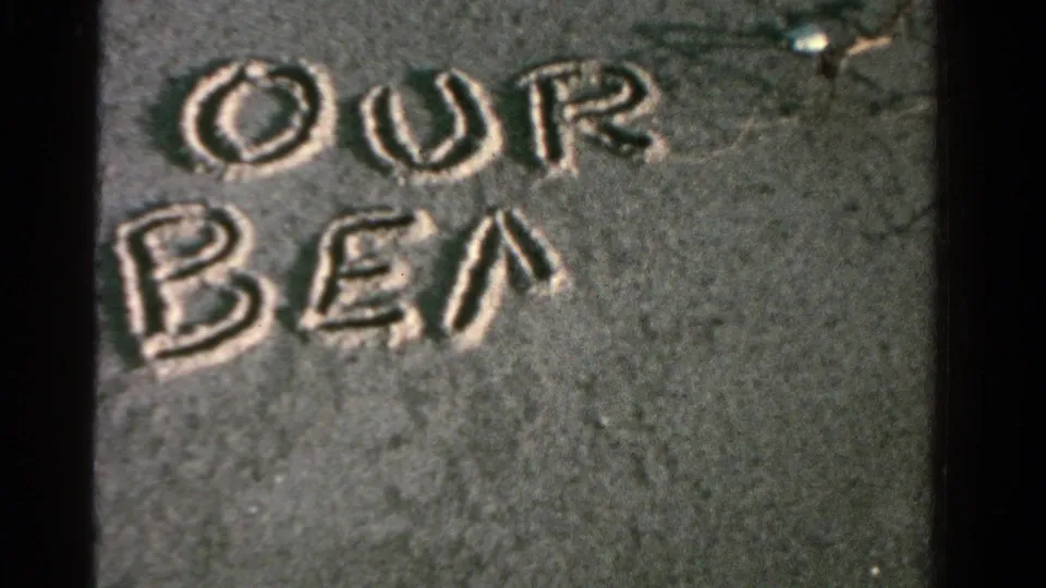 The beach message is partly formed, reading OUR BEA in large hand-drawn letters on wet sand.