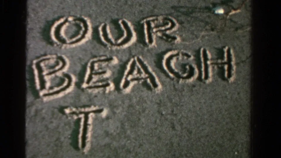 The words OUR BEACH are visible in wet sand, with an additional letter beginning below the main line.