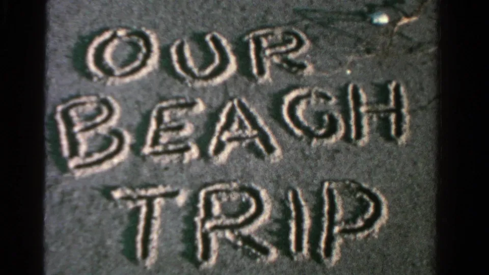 The sand title OUR BEACH TRIP remains in close-up, showing soft 8mm texture and uneven beach surface.