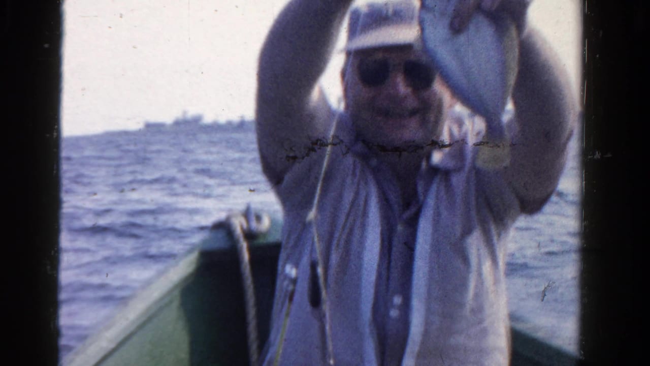 Man in sunglasses raises his hands while seated in a small boat on open water.