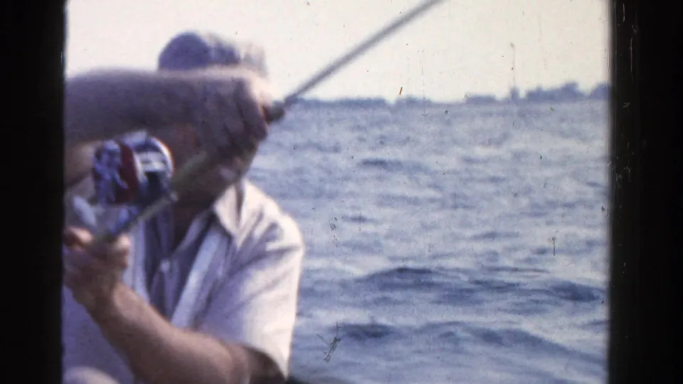 A man in a small boat grips a fishing rod and reel, with open Ontario water and low shoreline visible behind him.
