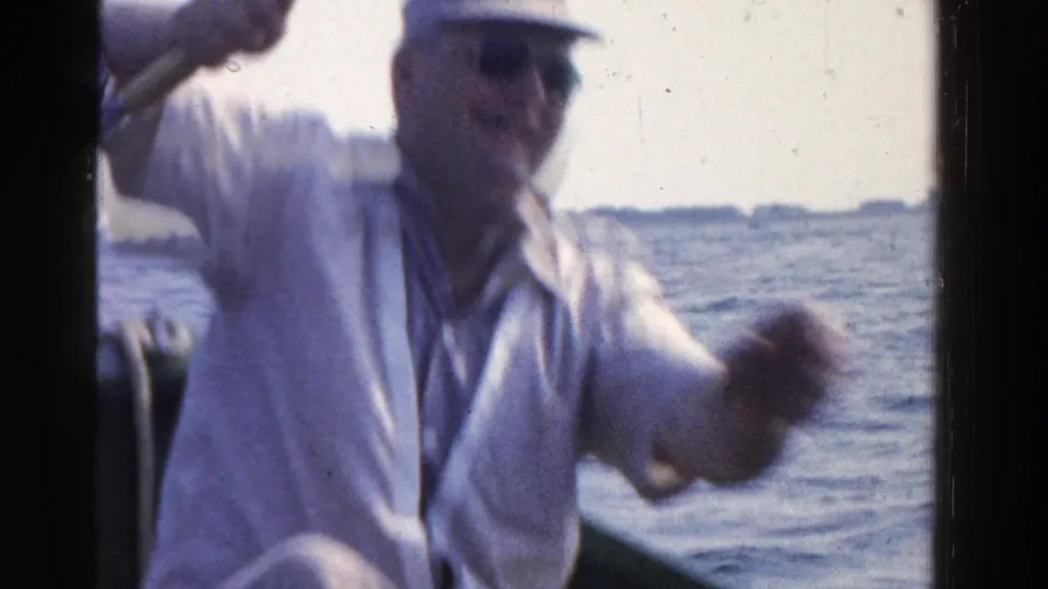 In 1958 Ontario home-movie footage, a man in a light shirt and cap fishes from a small boat on a calm lake.