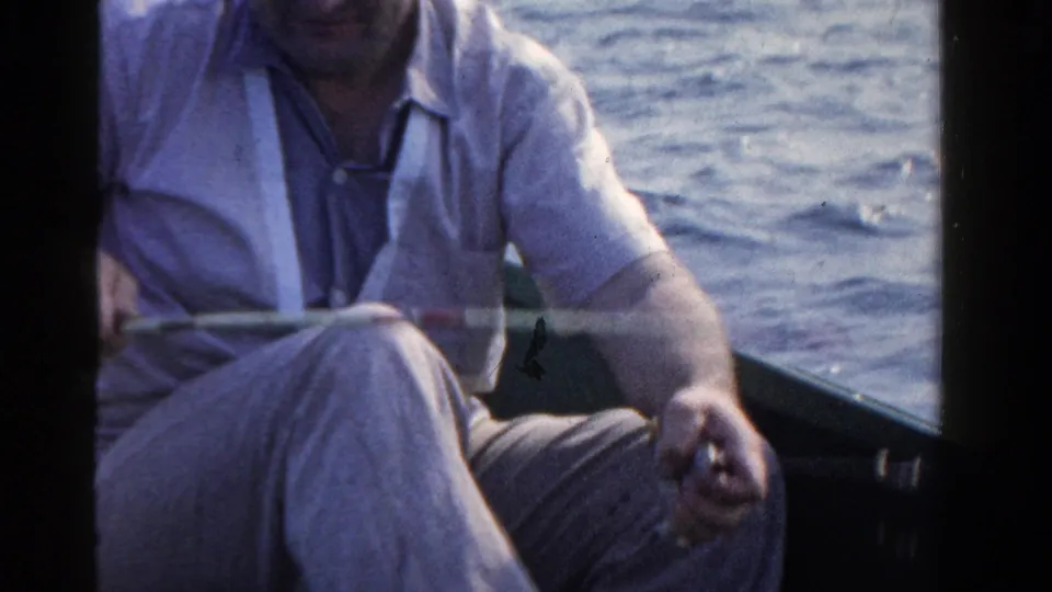 In the final frame, the man sits with the fishing rod across his lap in the small boat on the Ontario lake.