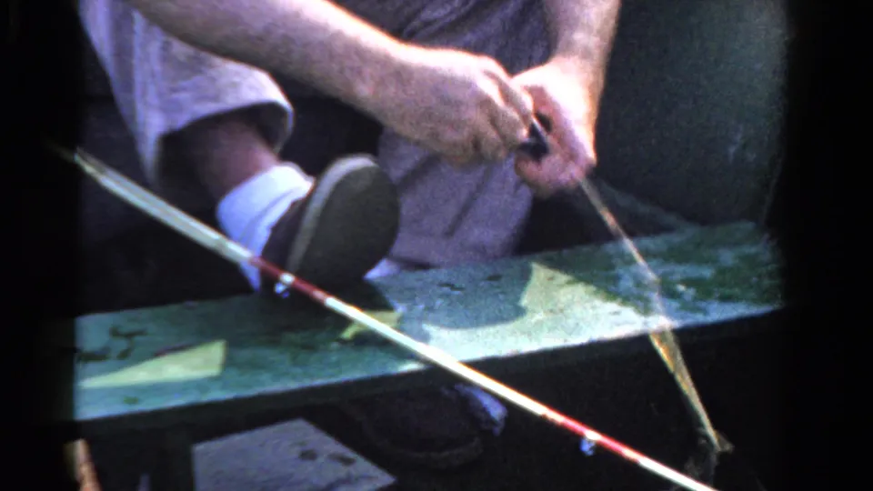 The 8mm frame shows a close view of a man handling fishing tackle in a green boat, with rod, line, shoe, sock, and trouser leg in view.
