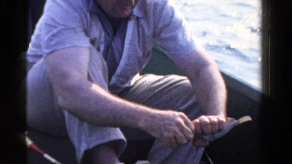 In this 8mm Ontario lake scene, the seated man grips the fishing rod handle while water glints in the background.