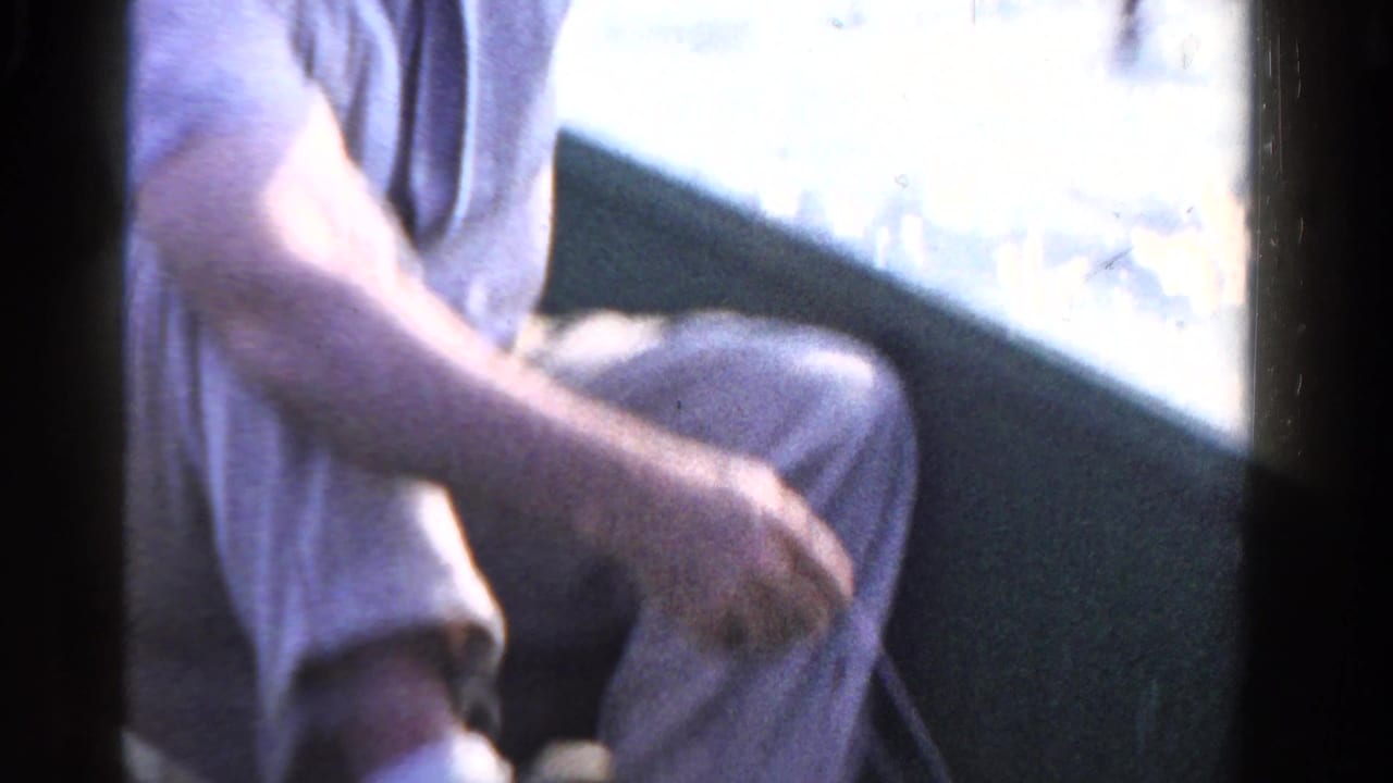 In Ontario home-movie footage from 1958, a man sits low in a small boat while handling a fishing line near bright lake water.