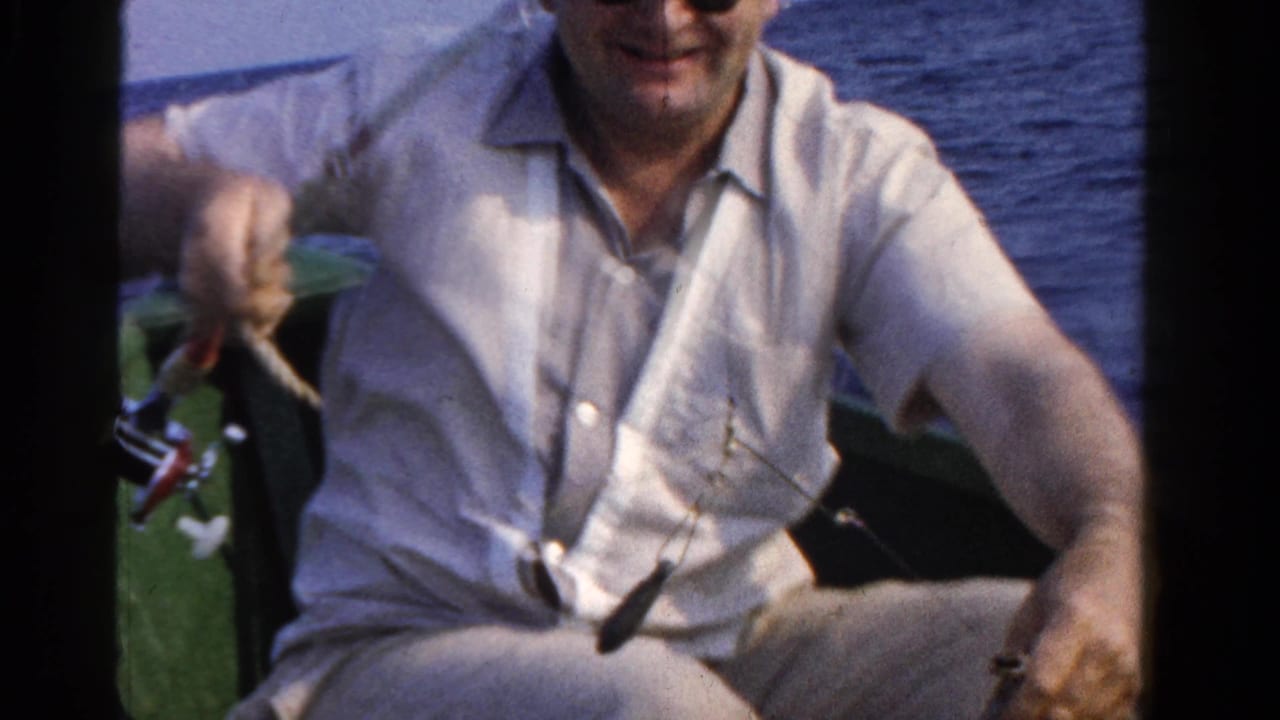 An older man in a small boat holds up fishing line and tackle, with open water behind him in the 1958 Ontario footage.