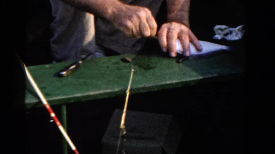 Close view of hands preparing the catch on a green boat surface, with a spoon and fishing rod visible in the 1958 Ontario home movie.