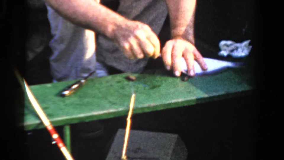 Hands handle a small fish on a green boat surface, with simple tools and fishing gear visible in the 1958 Ontario footage.