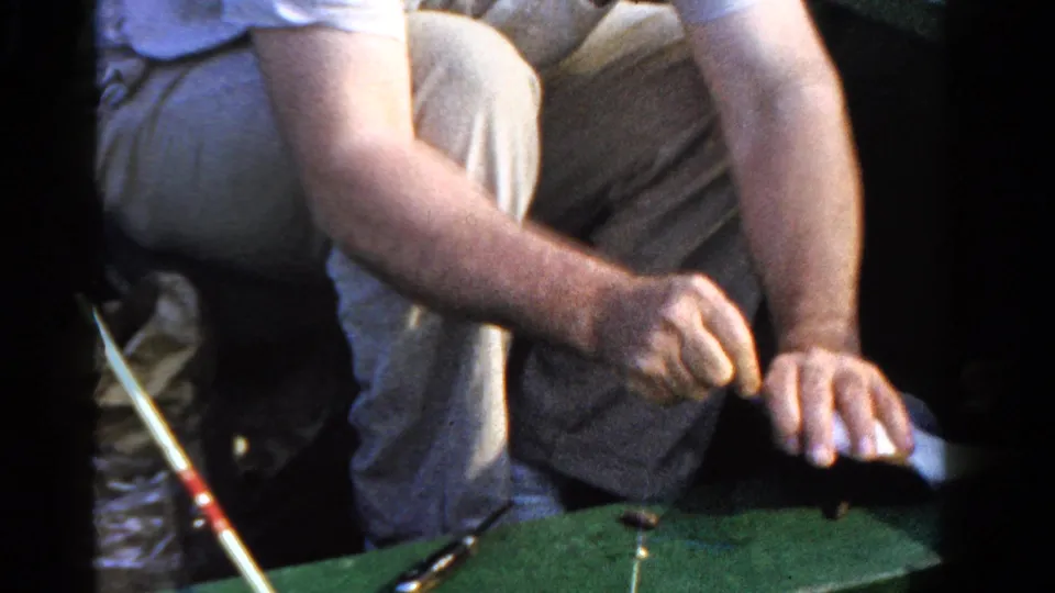 1958 Ontario 8mm frame showing the man’s hands returning to the green board area with fishing rod and small fish visible.