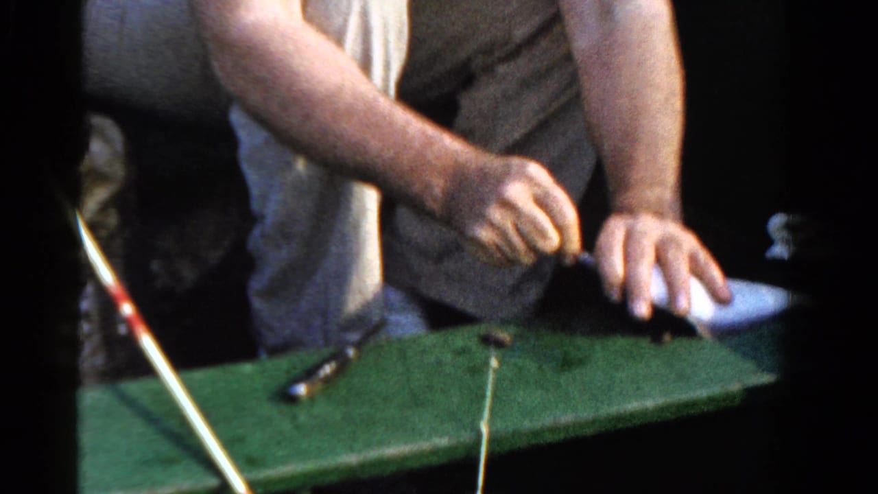 In 1958 Ontario home-movie footage, a seated man works fishing line over the green interior of a small boat.