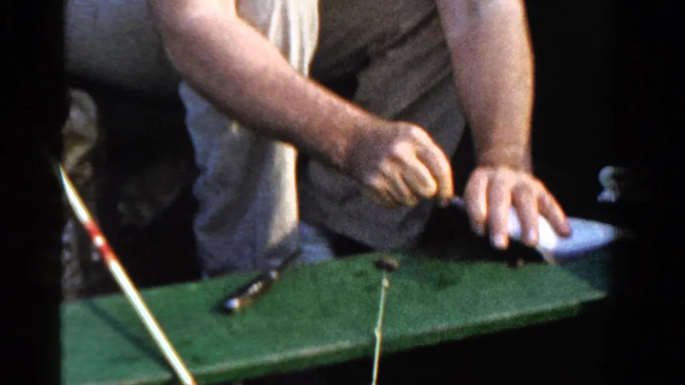In 1958 Ontario home-movie footage, a seated man works fishing line over the green interior of a small boat.
