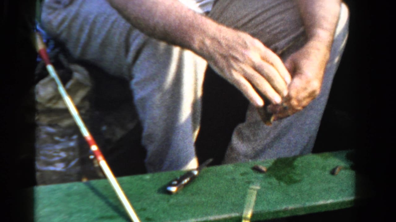 The man sits in a small boat in Ontario, Canada, handling fishing line or bait beside a rod and scattered tackle.
