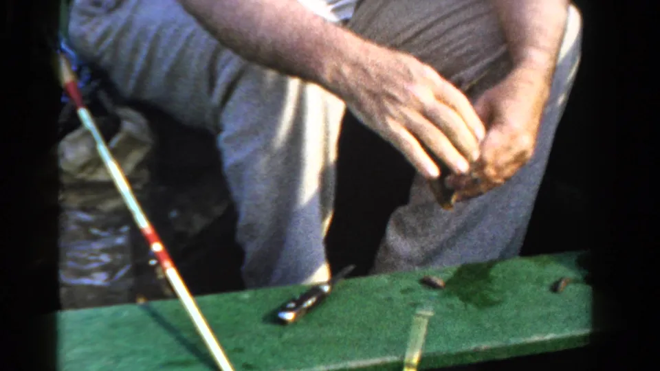 The man sits in a small boat in Ontario, Canada, handling fishing line or bait beside a rod and scattered tackle.