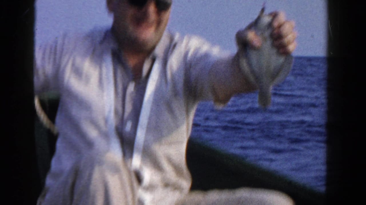 In 1958 Ontario home-movie footage, a man in a light shirt holds a small fish while seated on a boat.