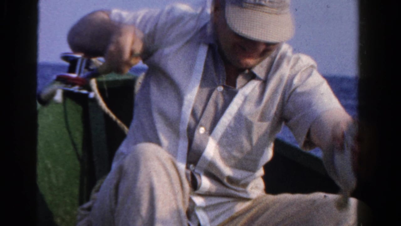 A man in a light cap and shirt sits low in a small boat on Ontario water, handling fishing gear.