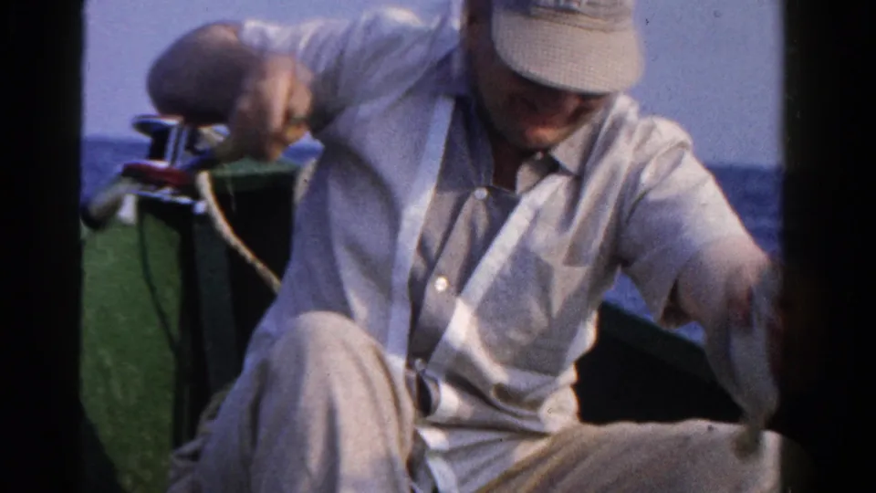 A man in a light cap and shirt sits low in a small boat on Ontario water, handling fishing gear.