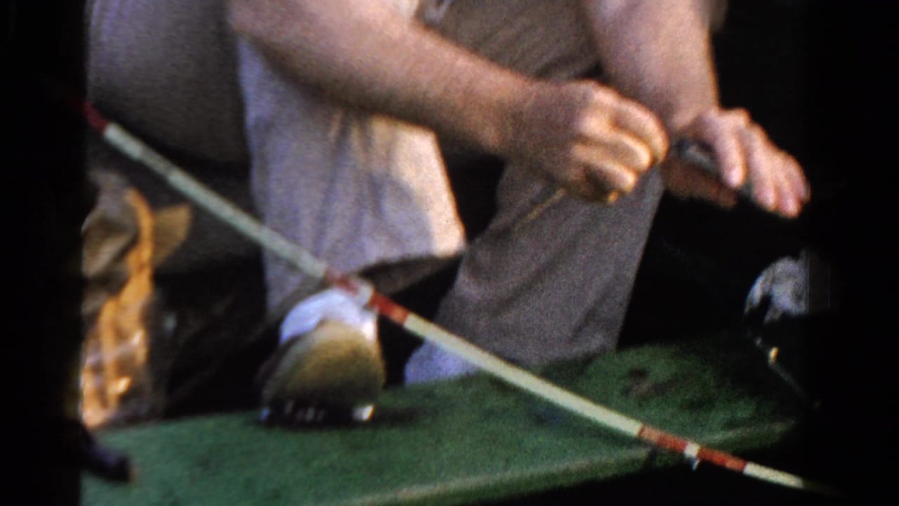 1958 Ontario home-movie frame showing a seated angler in light clothing working a fishing rod inside a small green boat.